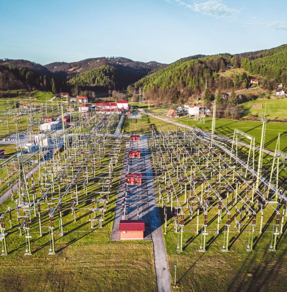 Electrical power substation in the country side of Slovenia. Fields and forests surrounding the power station in the suburbs. Aerial view.